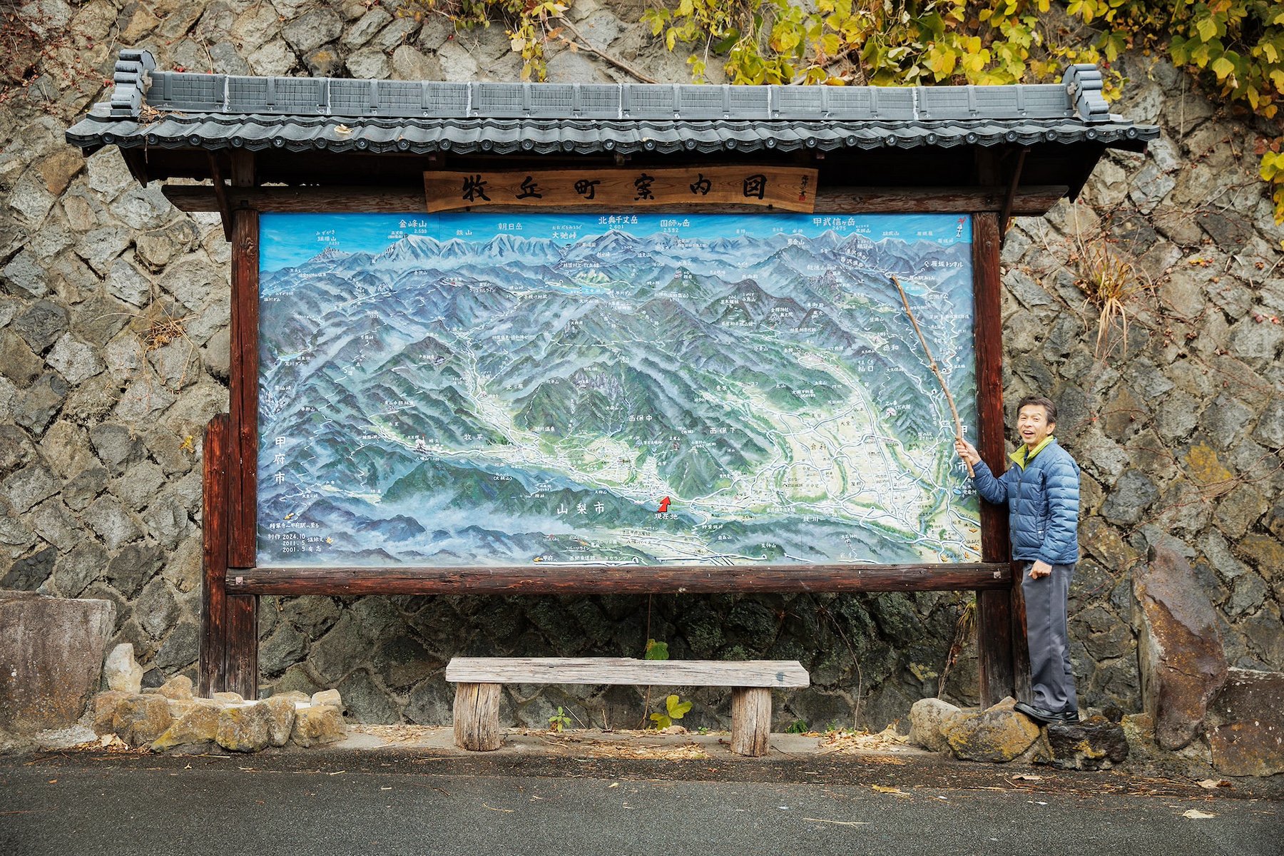 牧丘町西保地区の入り口に設置された案内図と、その横に立つ温井さん。