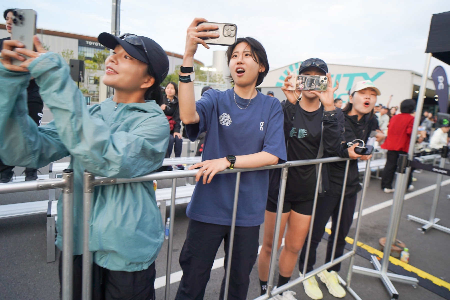 出走する番を終えて他ランナーの応援をするランナーたちが、スマートフォンで選手を撮影している。